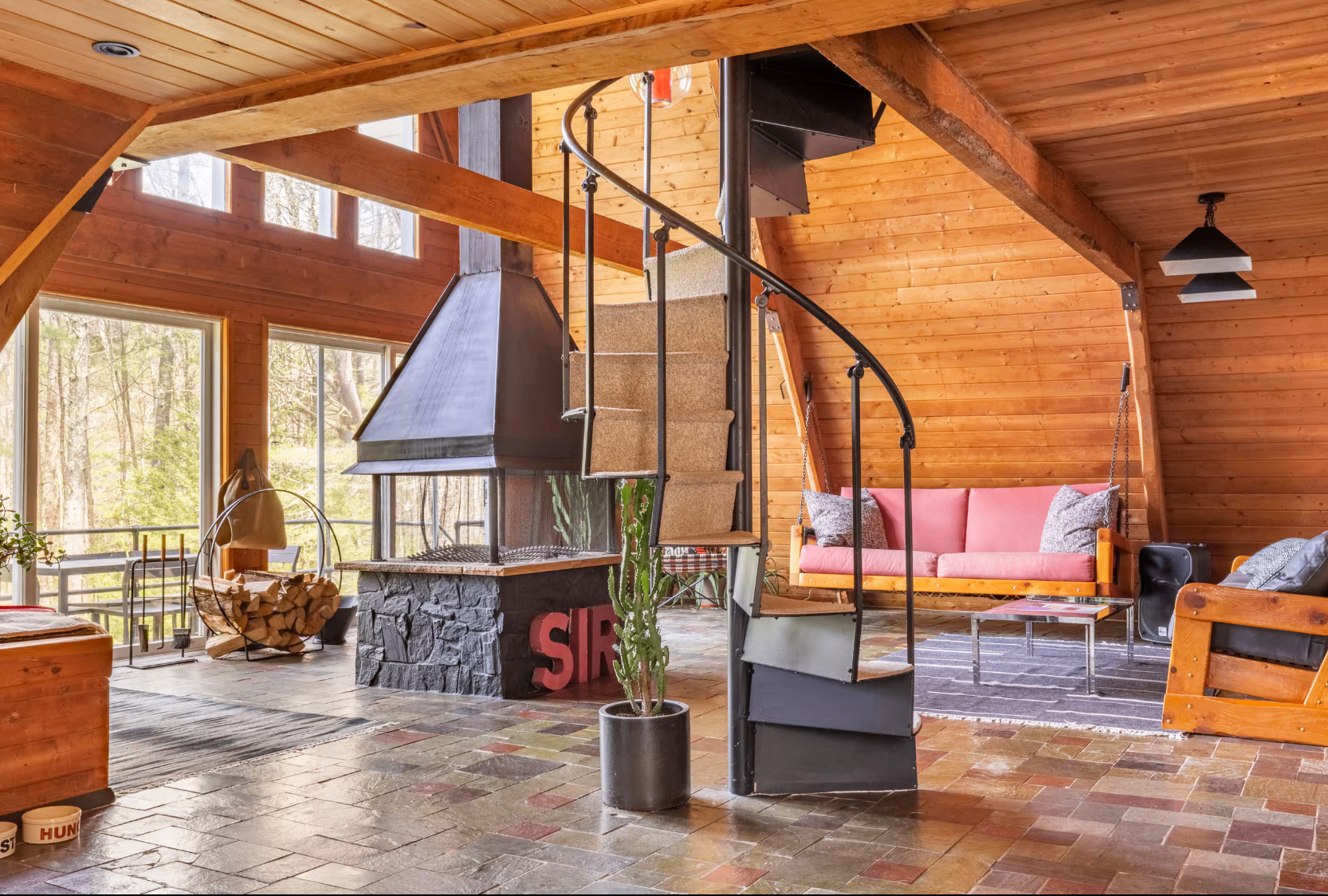 Interior of the A-frame with spiral staircase, wood stove, and pink sofa