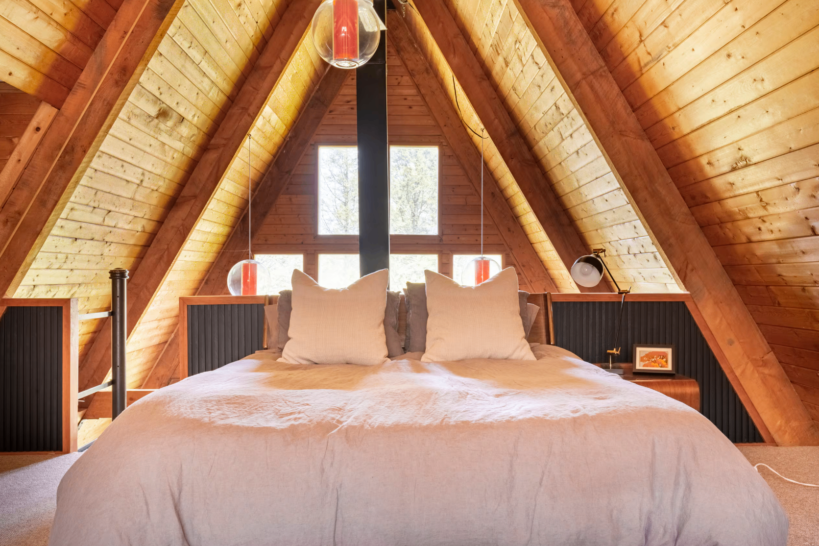 Loft bedroom under the A-frame peak with pendant lights and forest view